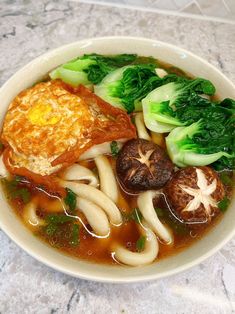 a white bowl filled with noodles, broccoli and other foods on top of a table