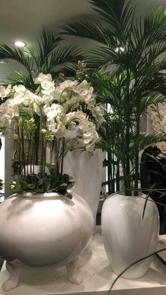 three white vases filled with flowers and greenery on top of a counter in a store