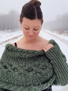 a woman wearing a green sweater standing in the snow with her hands on her shoulder