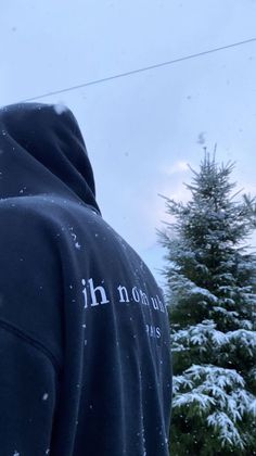 a person wearing a hoodie standing in front of a snow covered tree and power line