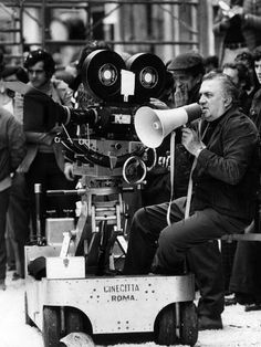 a man sitting on top of a cart next to a movie camera in front of a crowd