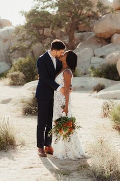 a bride and groom kissing in the desert with rocks behind them on their wedding day