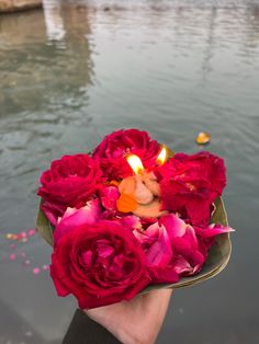 a person holding a candle and flowers in their hand near the water's edge