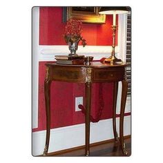 a small table with a vase on it in front of a red wall and window