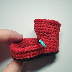 a hand holding a crocheted red slipper with a blue button on it