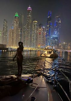 a woman standing on the back of a boat in front of a city at night