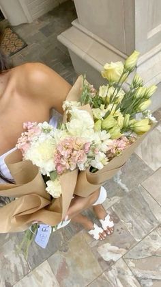 a woman holding a bouquet of flowers on the ground in front of a building with stone floors