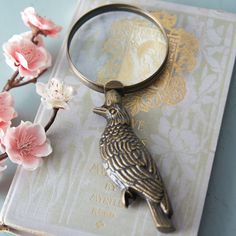 a bird keychain sitting on top of a book next to some pink flowers