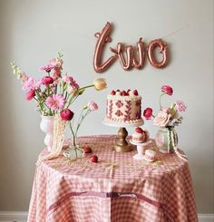 a table topped with a cake and pink flowers next to a balloon that says love