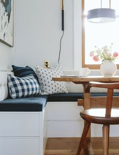 a room with a window seat, table and chair next to a vase filled with flowers