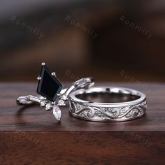 two wedding rings on top of a wooden table with diamonds and black stones in the middle