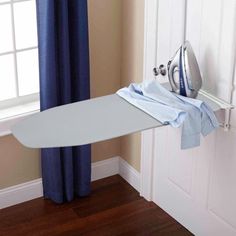 an ironing board is hanging on the wall next to a window with blue curtains