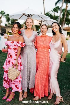 three women in dresses standing next to each other on the grass with an umbrella behind them