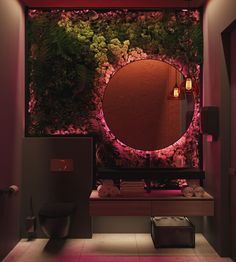 a bathroom with a mirror, toilet and plants on the wall behind it is lit by lights