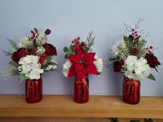 three red vases with white flowers and greenery in them sitting on a shelf