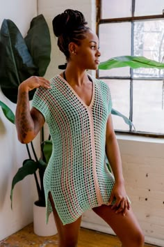 a woman standing in front of a window wearing a green crochet top and shorts