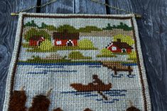 a cross - stitch bag hanging from a chain on a wooden fence with an image of boats and houses in the water