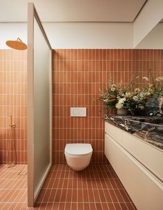 a bathroom with tiled walls and flooring has a toilet in the corner, along with flowers on the counter