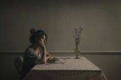 a woman sitting at a table in front of a vase with flowers