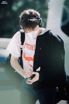 a person with headphones on walking and looking at his cell phone while wearing a t - shirt