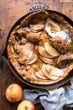 an apple cobbler pie in a cast iron skillet on a wooden table with apples around it