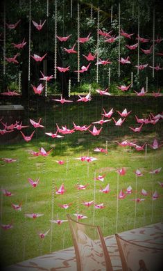 pink origami cranes are suspended from strings in the air over a green lawn