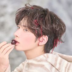 a young man is eating an apple while wearing a sweater and holding something in his mouth