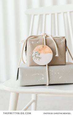 two wrapped presents sitting on top of each other next to a white chair with a round tag