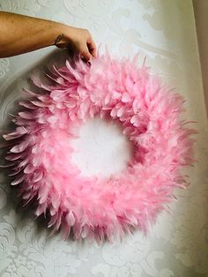 a pink feather wreath being held by someone's hand on top of a table