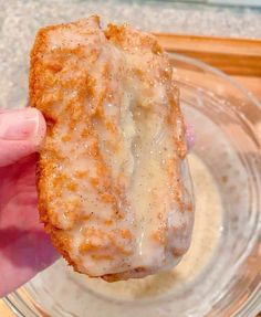 a person holding up a donut with icing on it in a glass bowl