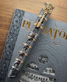 a fountain pen sitting on top of a book with gold trimmings and an ornate design