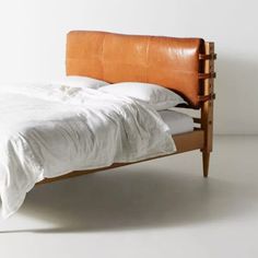 the bed is made up with white linens and wooden headboard, along with an orange leather pillow