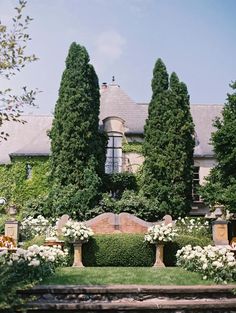 a large house surrounded by trees and white flowers in front of some water fountains