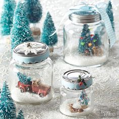 three glass jars filled with snow and small trees in the background, one has a christmas scene inside