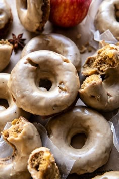 there are many doughnuts with icing and an apple in the back ground