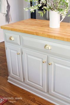 a kitchen island with white cabinets and wood counter tops in front of a potted plant