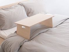 a bed with two pillows and a wooden table on top of it in front of the headboard