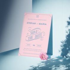 a pink save the date card sitting on top of a table next to a tree