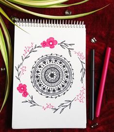 a notebook with a drawing on it next to two pens and a flowered design