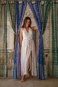 a woman wearing a white dress standing in front of blue and green drapes with her hands on her hips