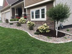 landscaping in front of a house with rocks and flowers on the lawn, including shrubs