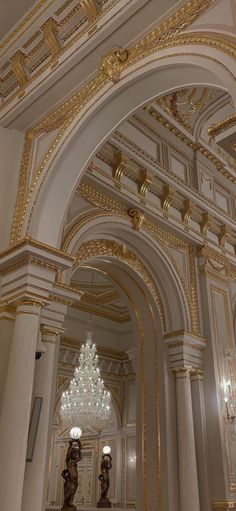 an ornate hallway with chandelier and marble columns in a building that looks like it has been painted gold