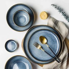 a table setting with blue plates, silverware and lemon wedges on the side