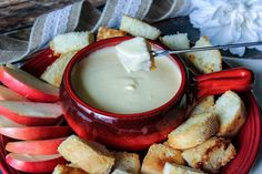 a red plate topped with apples and croutons next to a bowl of dip