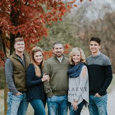 a group of people standing next to each other in front of a tree with red leaves