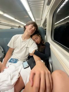 two people sitting on a train with their arms around each other and one person leaning against the wall