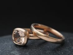 two gold wedding rings with an morganite stone in the center on a black background