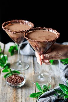 two glasses filled with chocolate martinis sitting on top of a wooden table next to green leaves