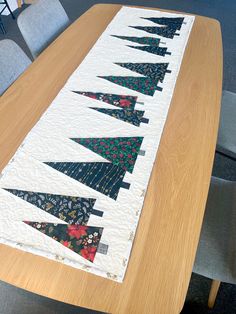 a wooden table with a quilted christmas tree runner on it's edge and chairs in the background