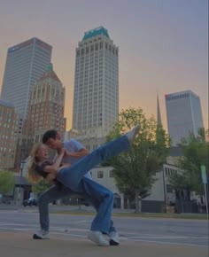 a man and woman are dancing in front of some tall buildings at sunset or dawn